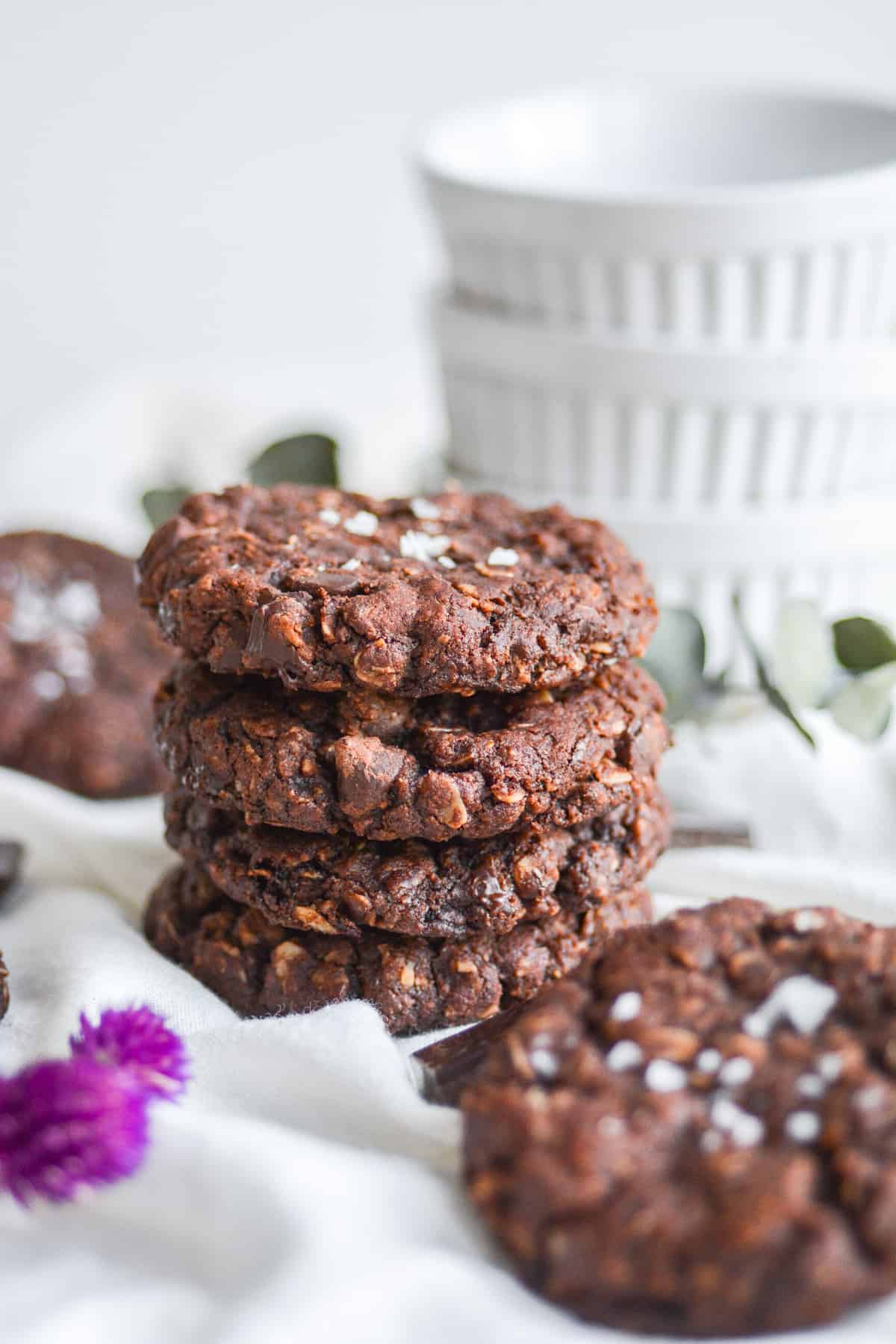 A stack of four Vegan Chocolate Oatmeal Cookies on a white cloth.