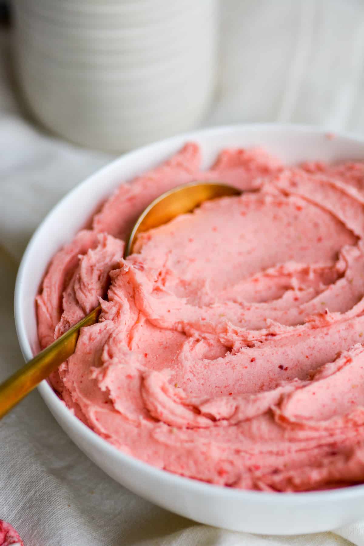 Vegan Strawberry frosting in a bowl with a gold spoon