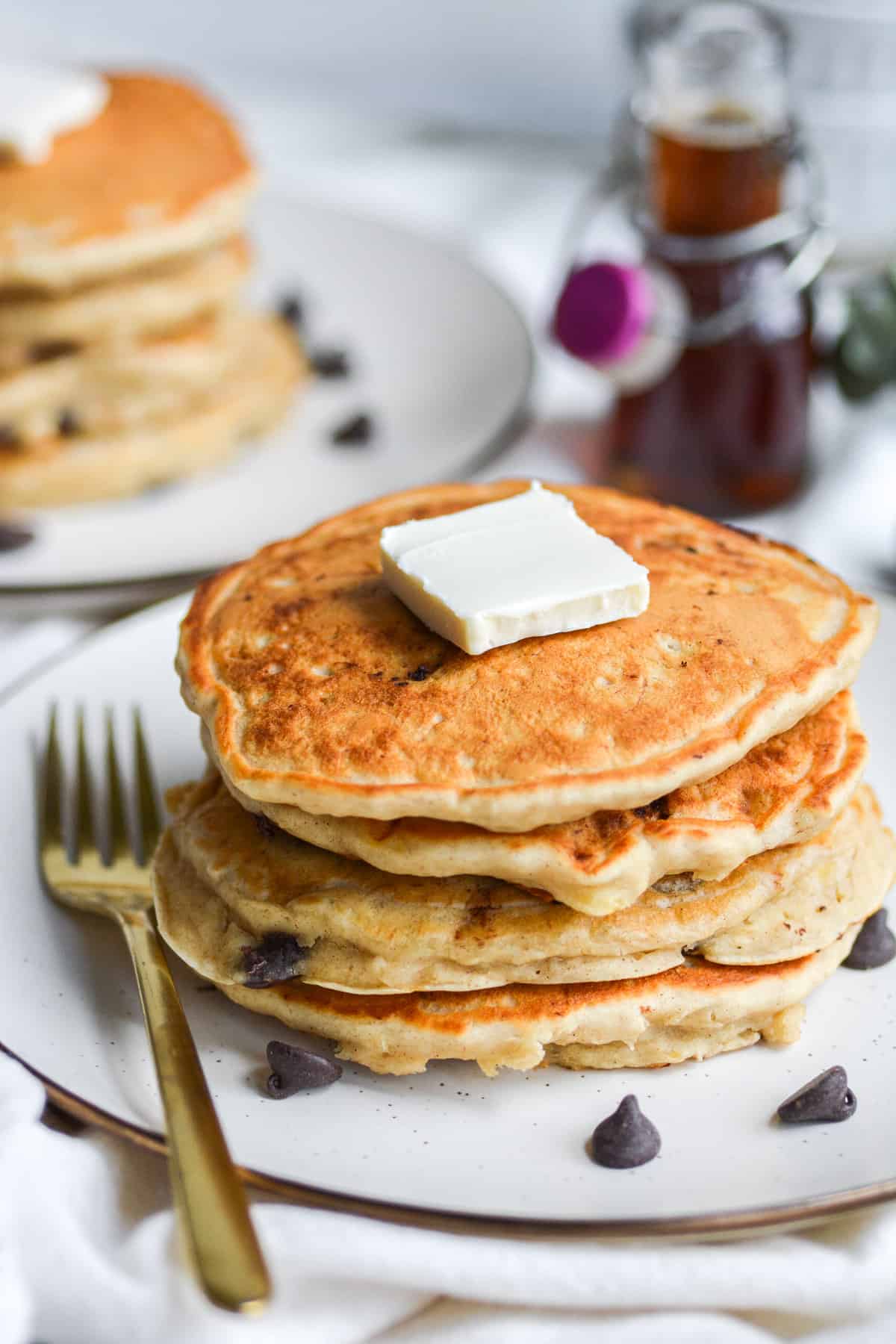 A stack of four pancakes on a plate with a pat of butter on top
