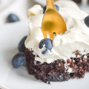 Fork in a piece of chocolate blueberry skillet cake topped with whipped cream and blueberries.