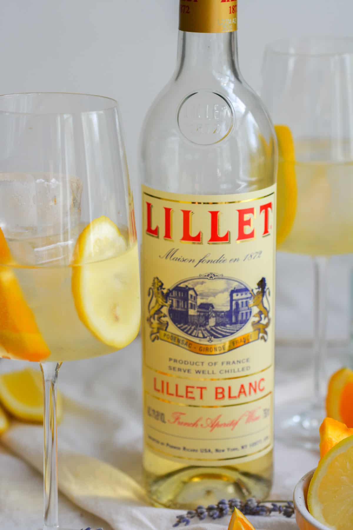 A bottle of Lillet next to two wine glasses of spritz