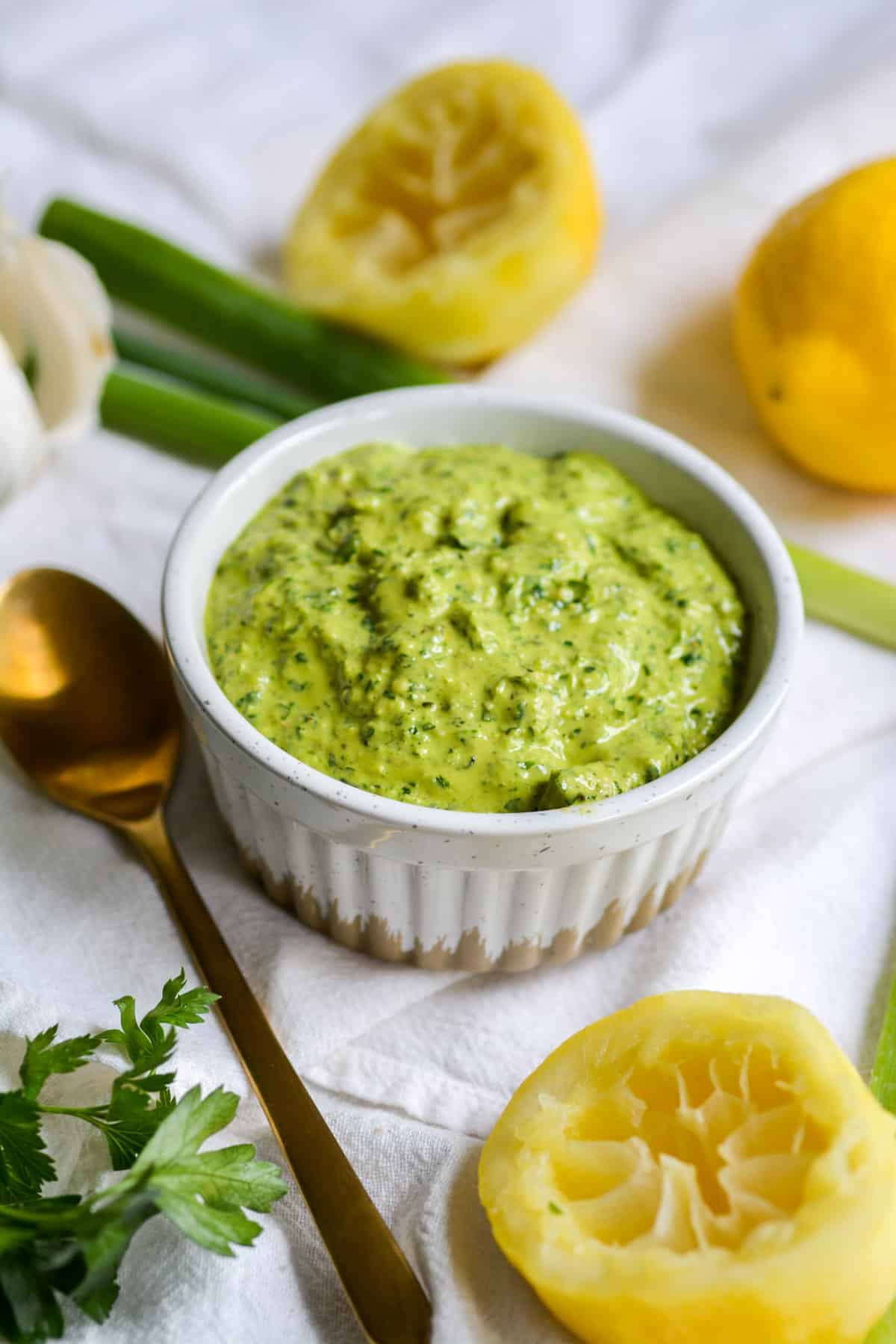 Vegan scallion and parsley pesto in a bowl with lemon and parsley in the fore ground