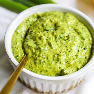 close up of vegan parsley scallion pesto in a small bowl with a gold spoon in it