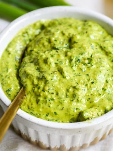 close up of vegan parsley scallion pesto in a small bowl with a gold spoon in it