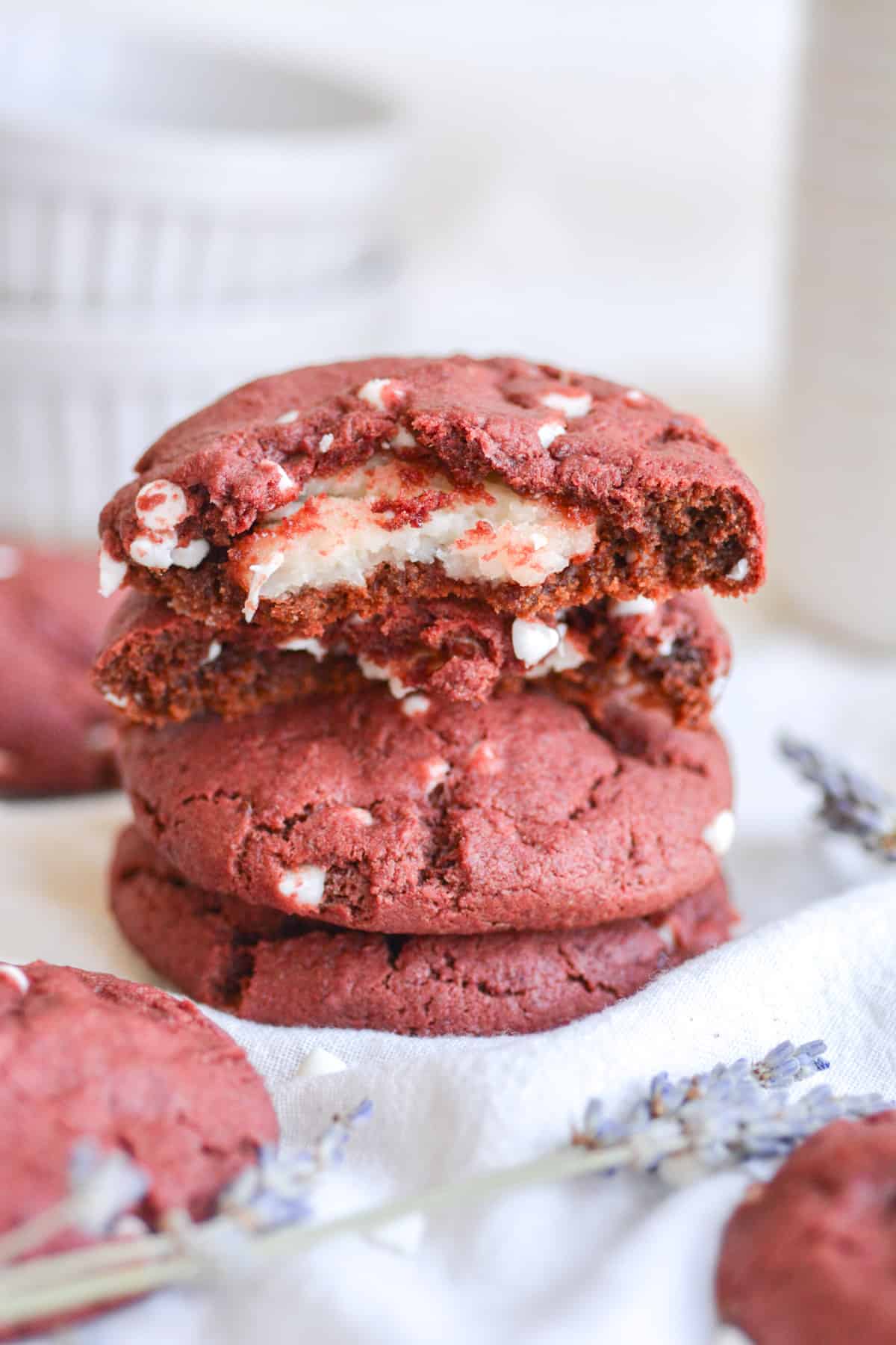 A broken open vegan cheesecake stuffed red velvet cookie on top of a stack of cookies