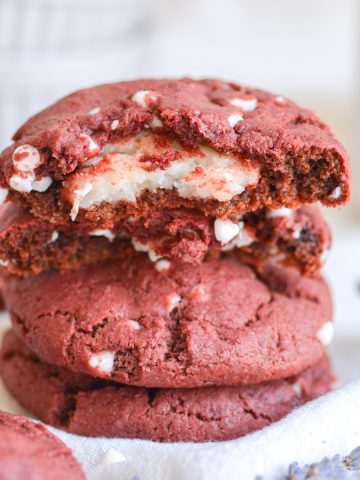 A broken open vegan cheesecake stuffed red velvet cookie on top of a stack of cookies