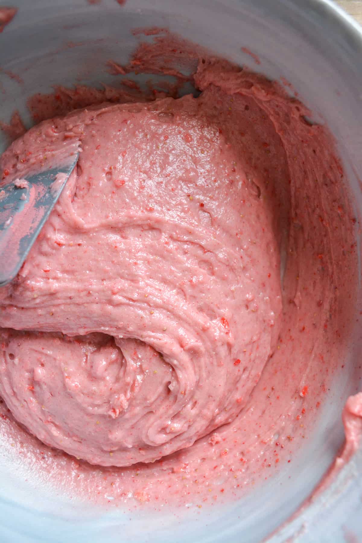Strawberry cupcake batter in a mixing bowl with a rubber spatula toward the left of the bowl.