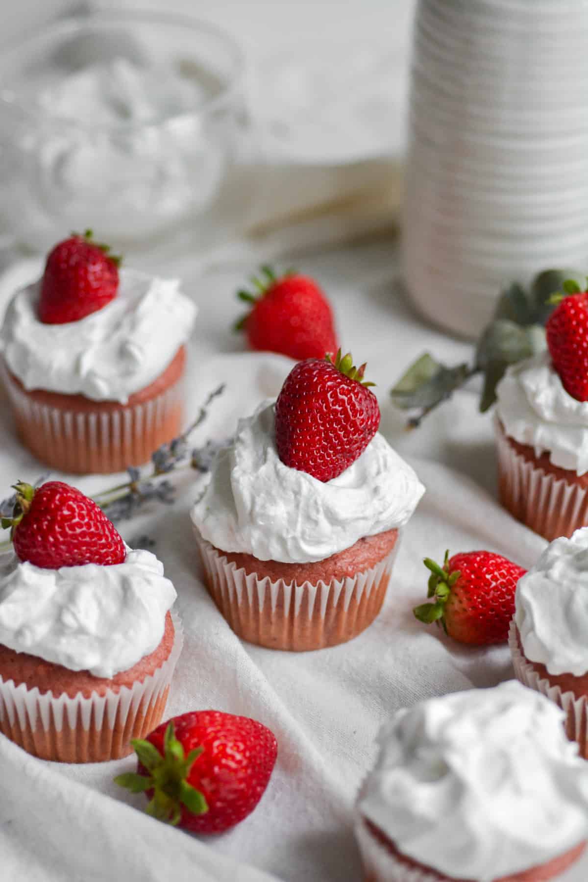 Vegan Strawberry and cream cupcakes topped with strawberries on a white cloth