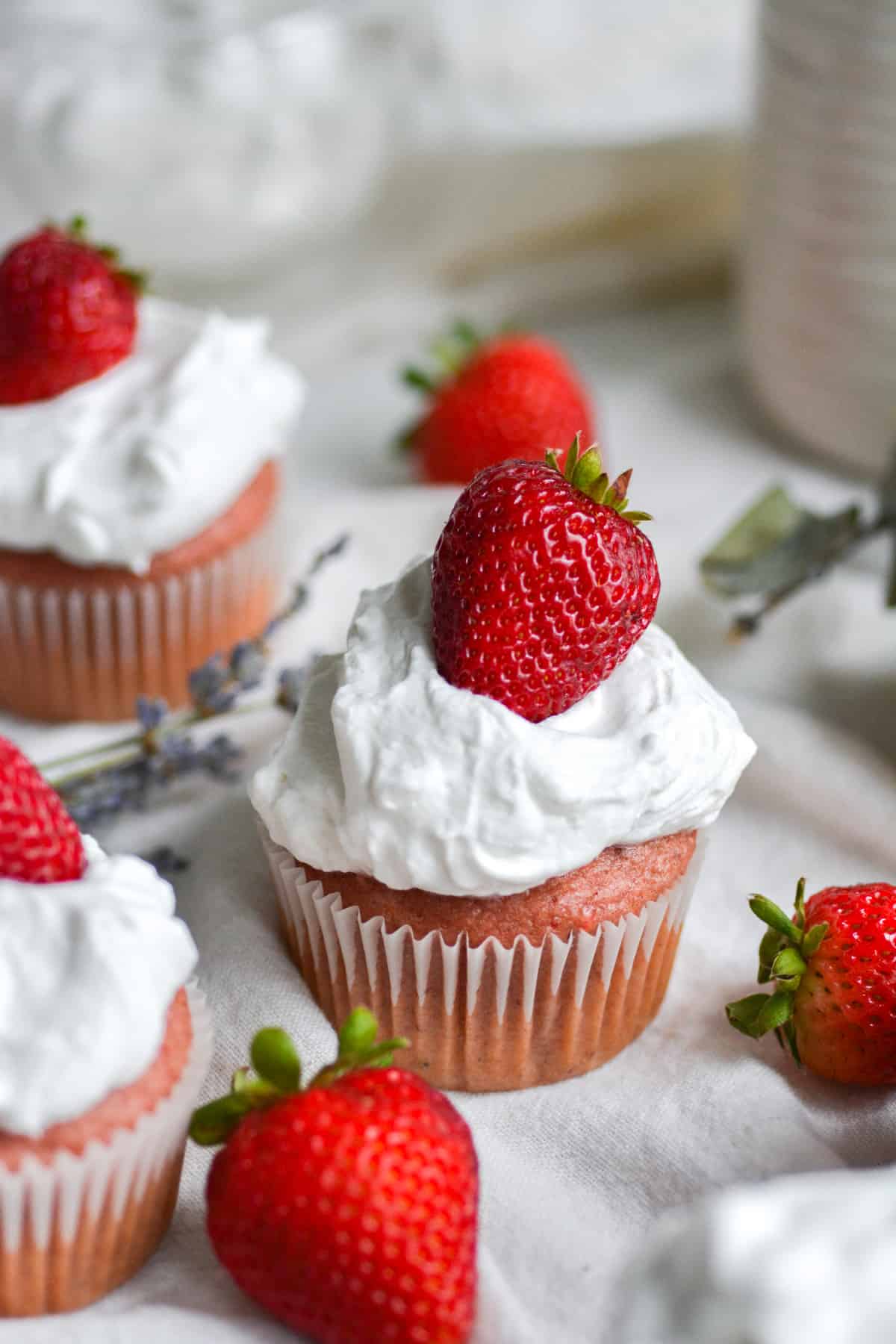 A vegan strawberry cupcake topped with a dollop of whipped cream and a fresh strawberry/