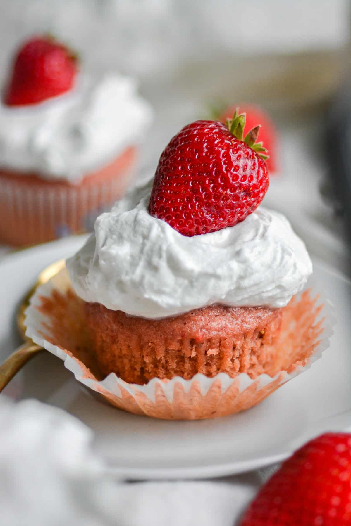 Vegan Strawberry Cupcakes topped with chipped cream and a fresh strawberry sitting in the cupcake wrapper.