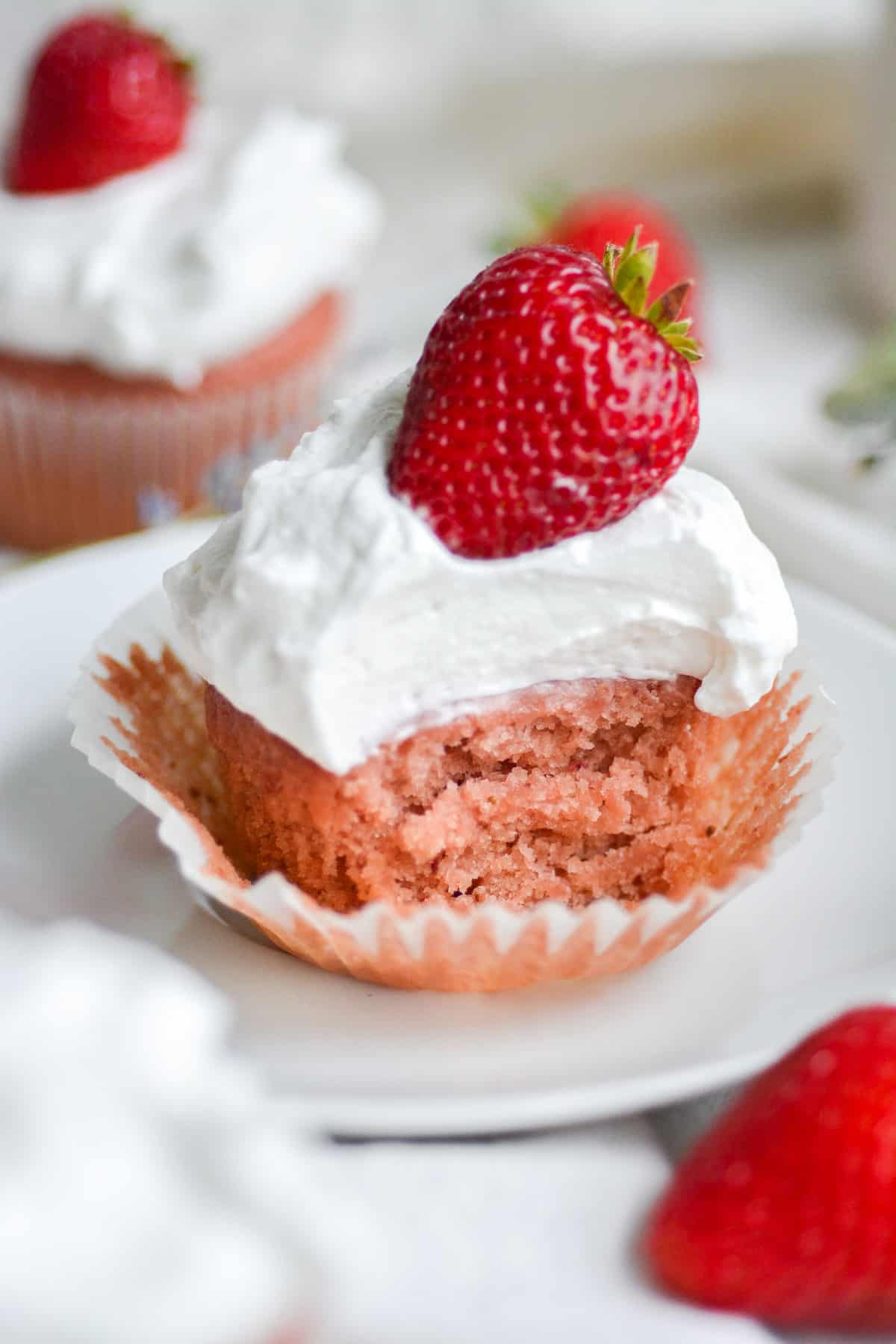 A bite taken out of a vegan strawberry and cream cupcake