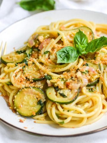 A plate of vegan zucchini pasta wuth a gold fork next to it