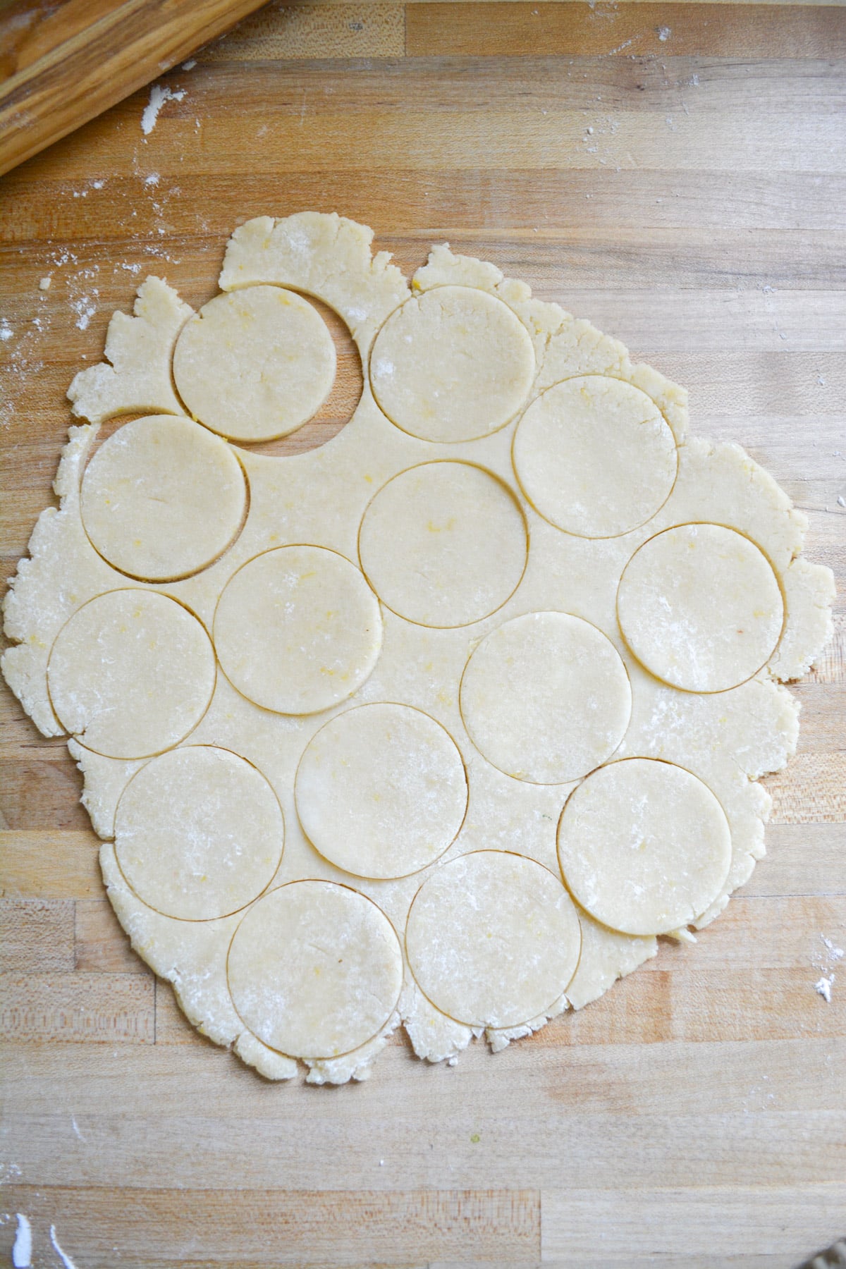 Dough rolled out on a wooden surface with circles cut out of it.