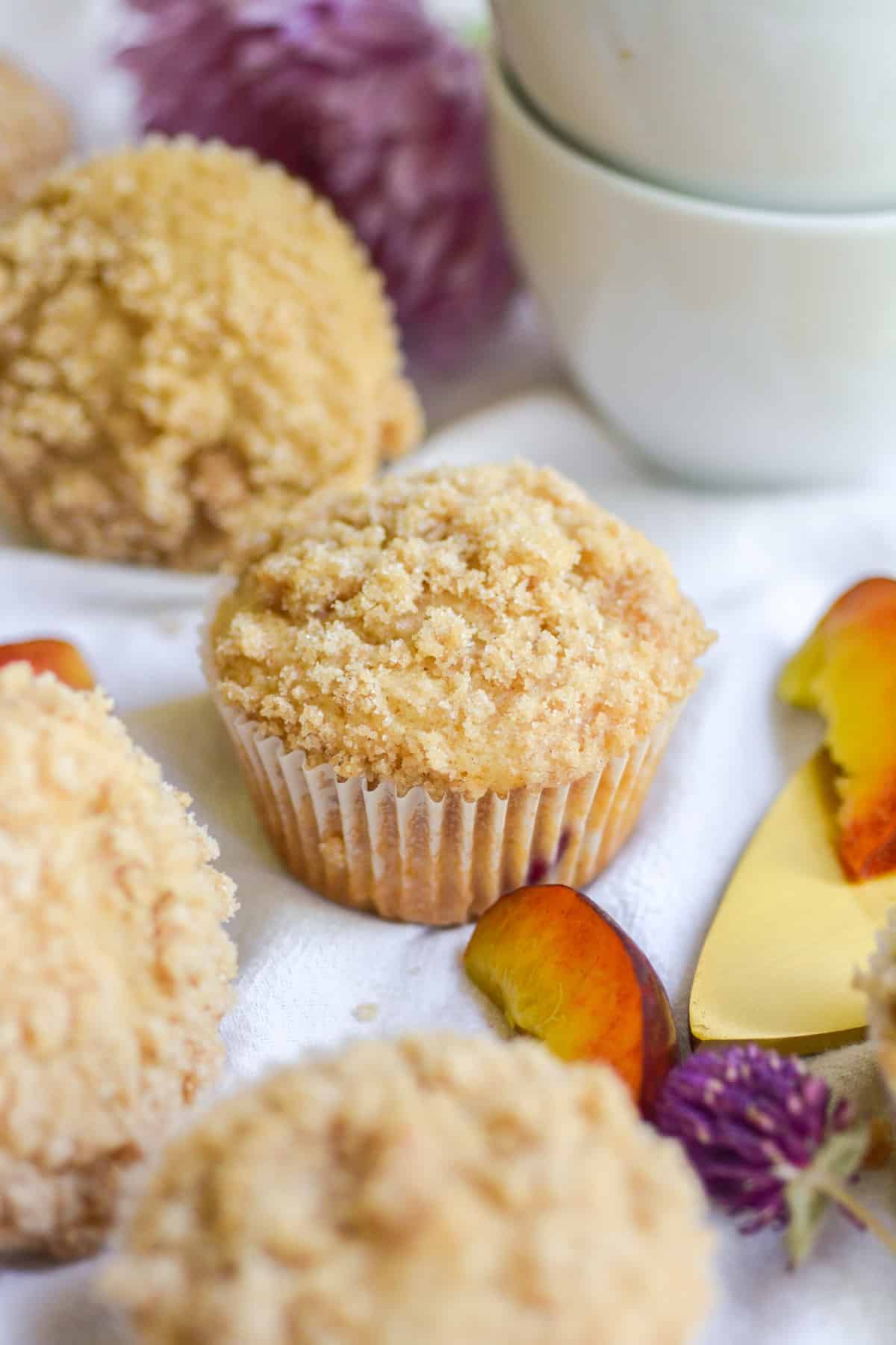 Muffins on a white cloth with peaches in the foreground