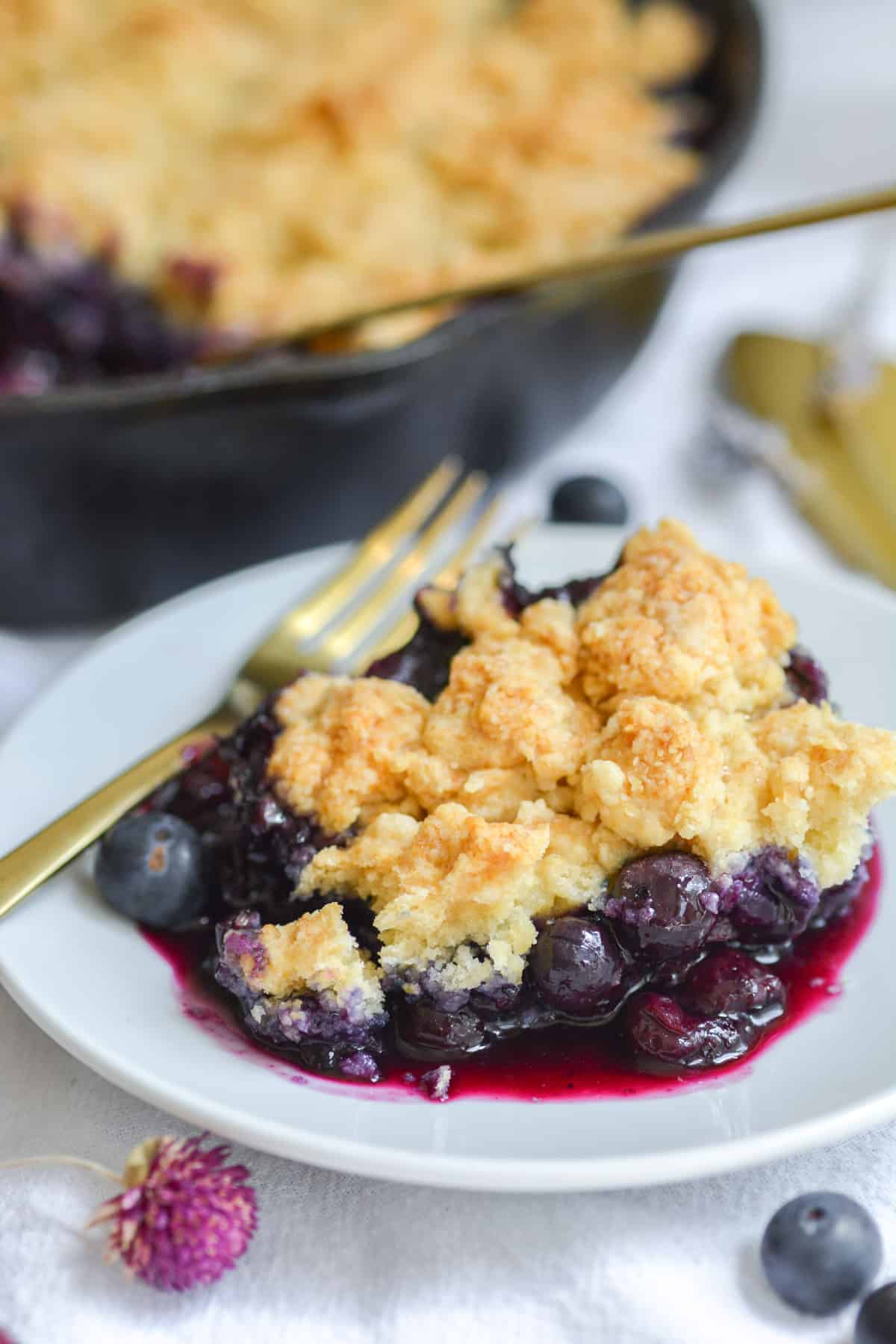 A scoop of vegan blueberry cobbler on a white plate with a gold fork.
