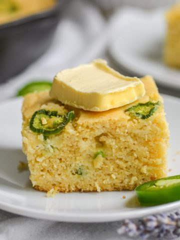 a square slice of eggless cornbread on a white plate topped with a pat of butter.