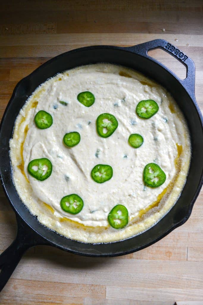 batter added into a cast iron skillet topped with jalapenos.