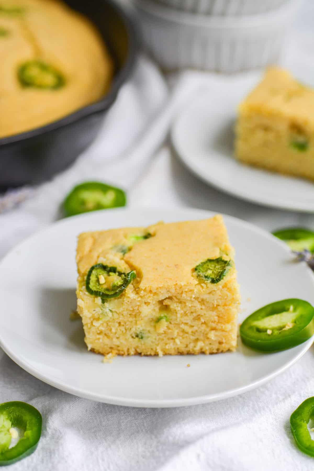 slice of vegan jalapeño cornbread on a white plate with a slice on jalapeno