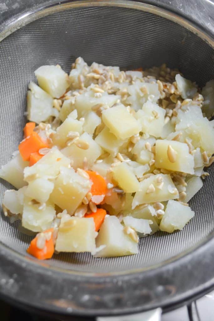 Cooked potato, carrot and sunflower seeds in a mesh strainer