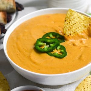 Nut free vegan queso in a bowl with a chip in it.