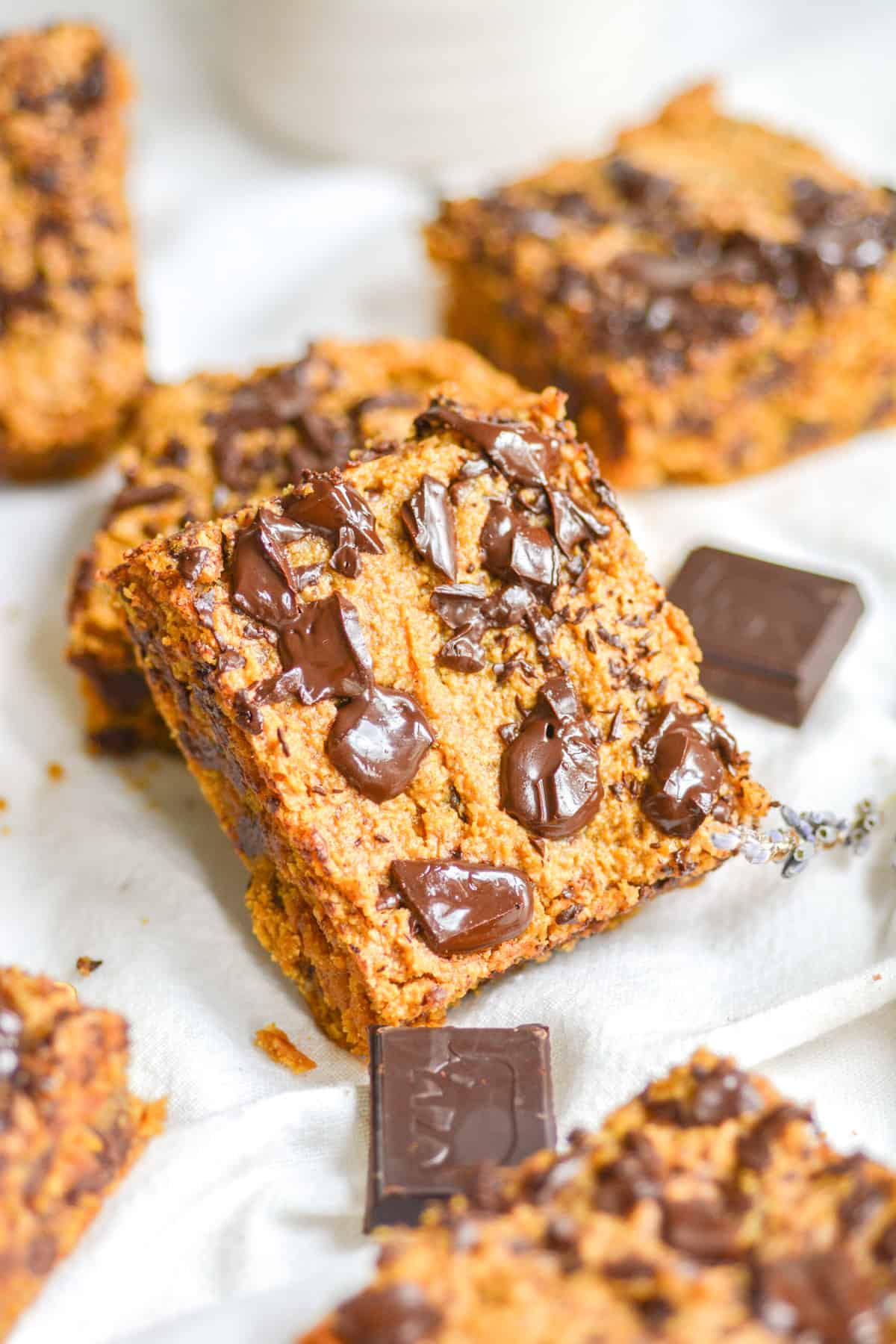 cashew butter blondies leaning on another blondie on a white cloth with squares of chocolate in the scene.