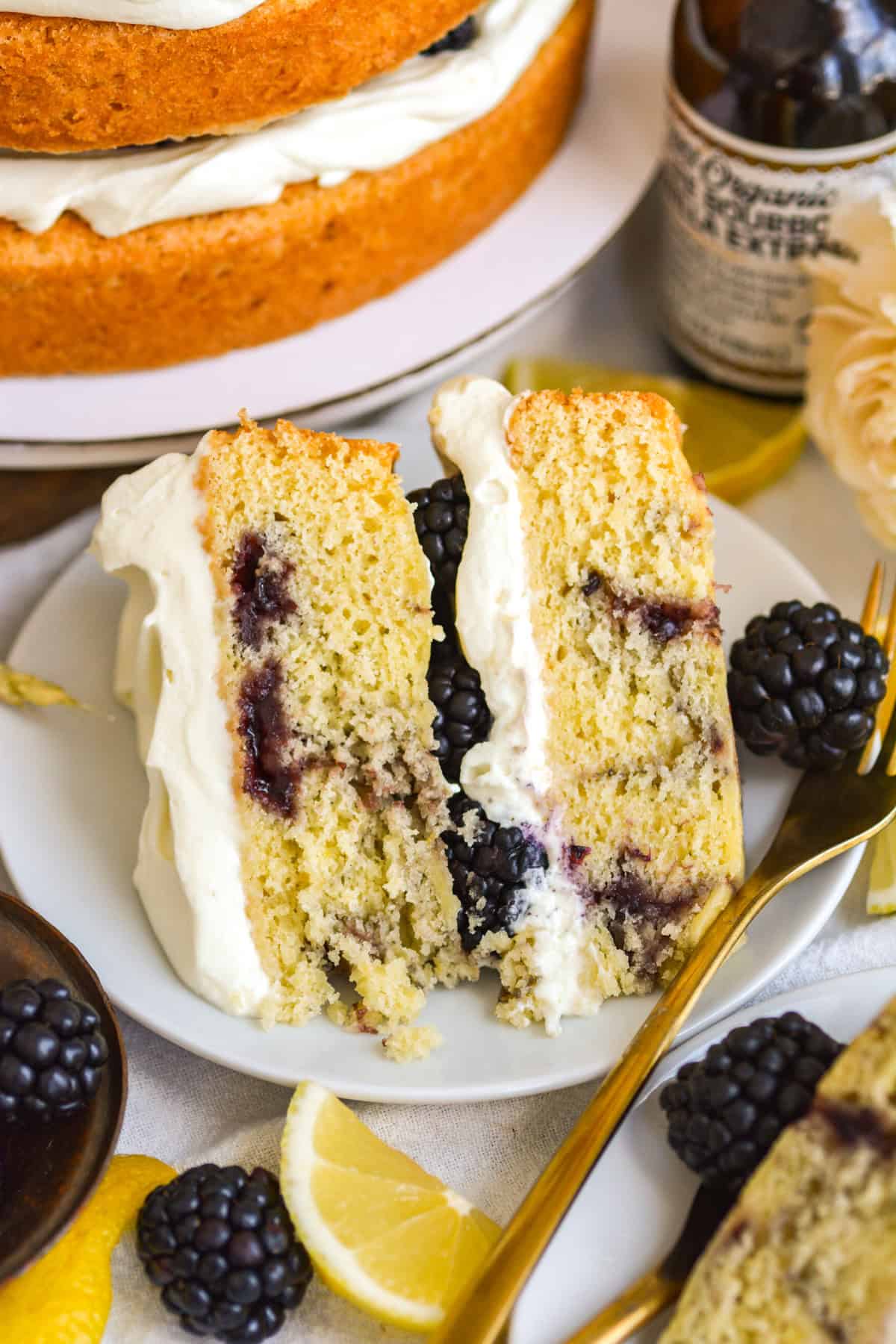 A slice of Vegan Blackberry Chantilly Cake on a white plate with a gold fork.