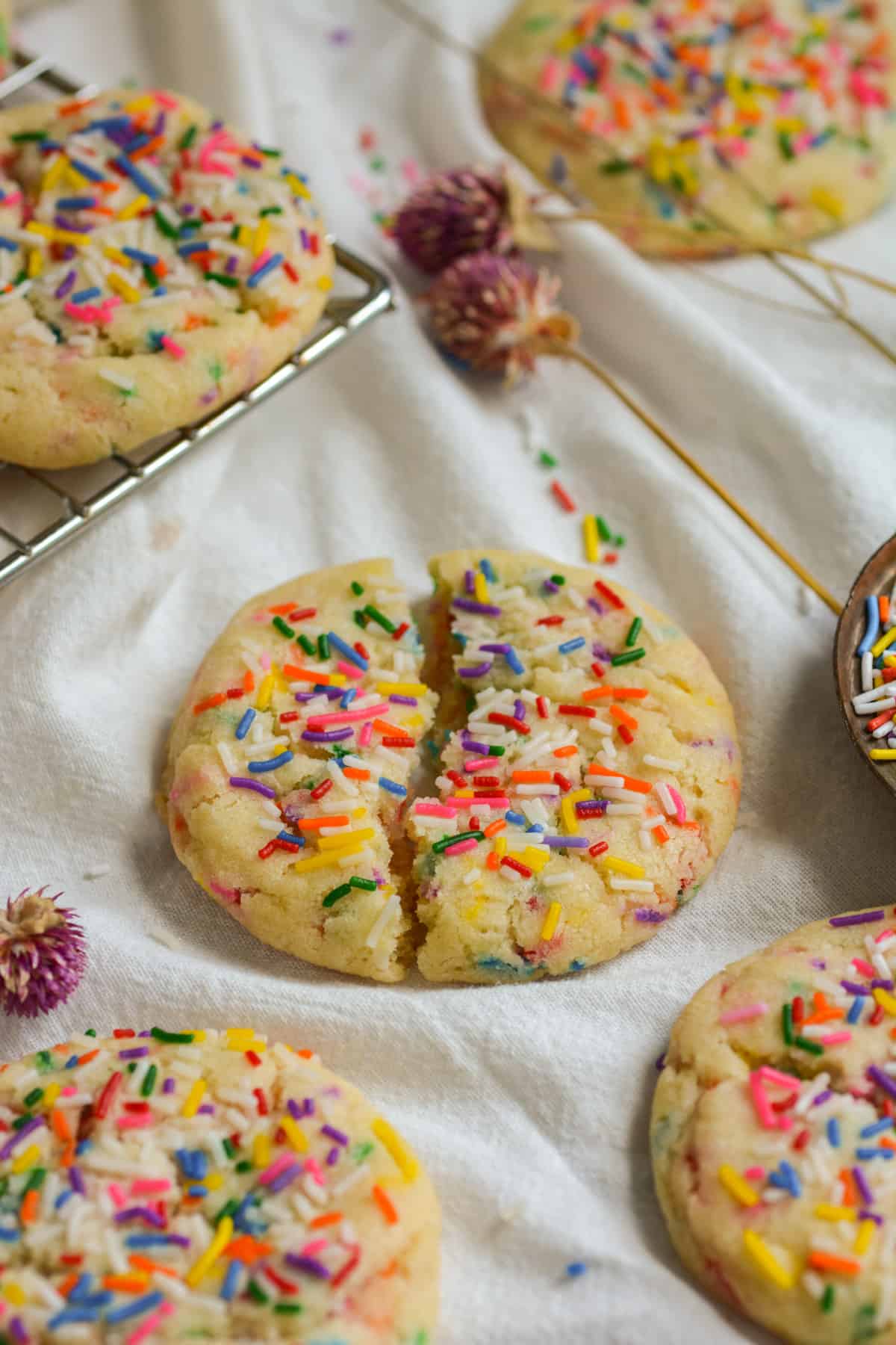 An eggless vegan funfetti sprinkle cookie broken in half on a white cloth.