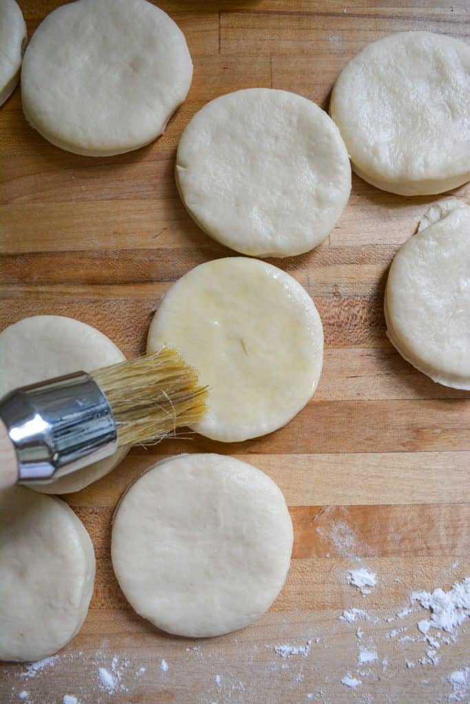a brush brushing a dough circle with butter