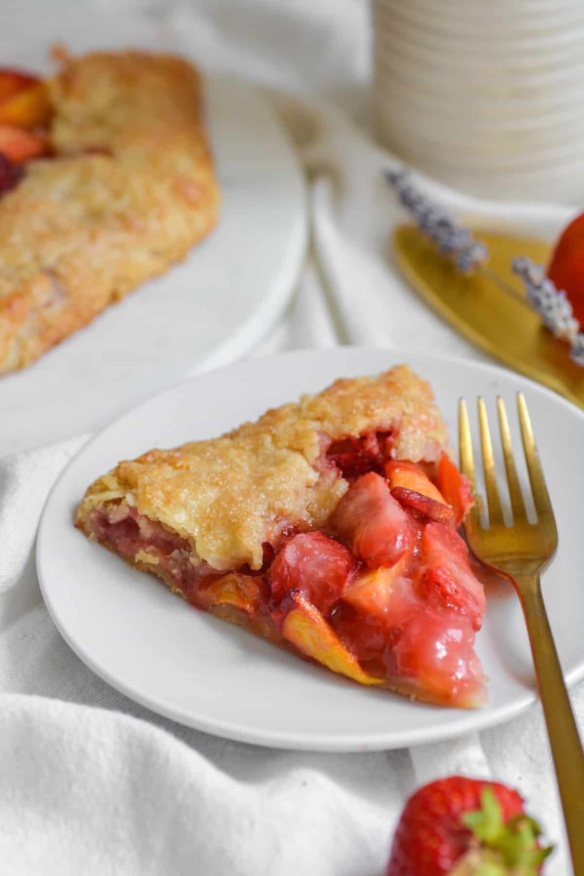 A slice of Vegan Strawberry peach galette on a white plate with a gold fork.