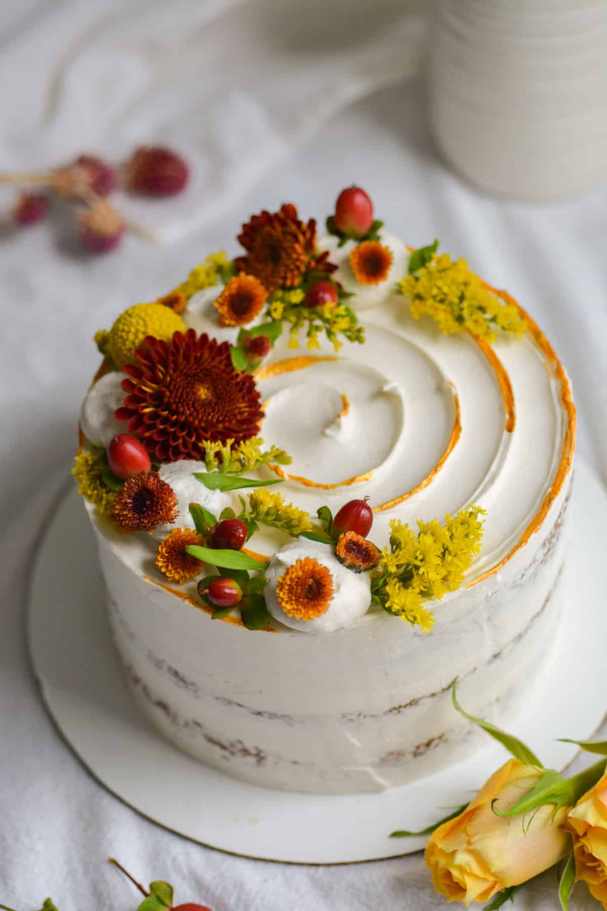 The frosted vegan apple spice cake decorated with maroon and yellow flowers.