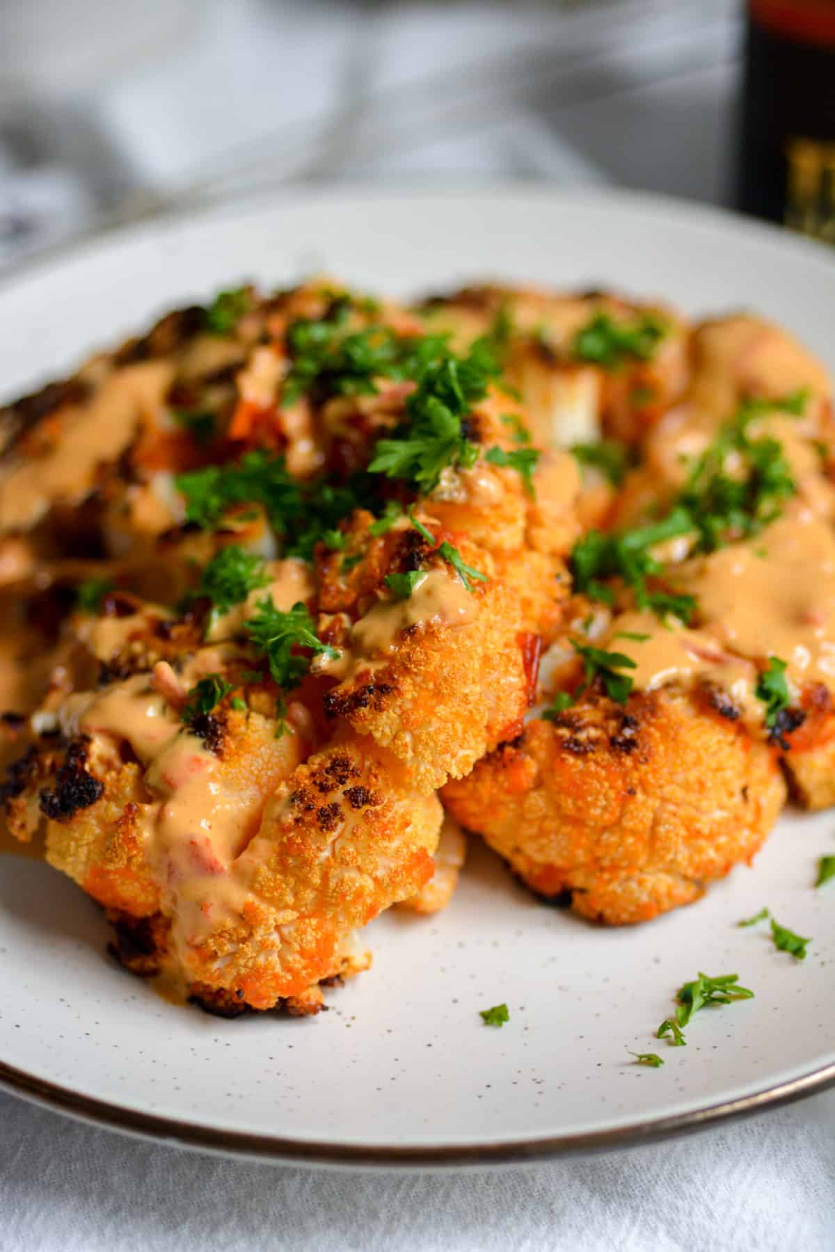 Two vegan harissa butter roasted cauliflower steaks on a plate with parsley on top