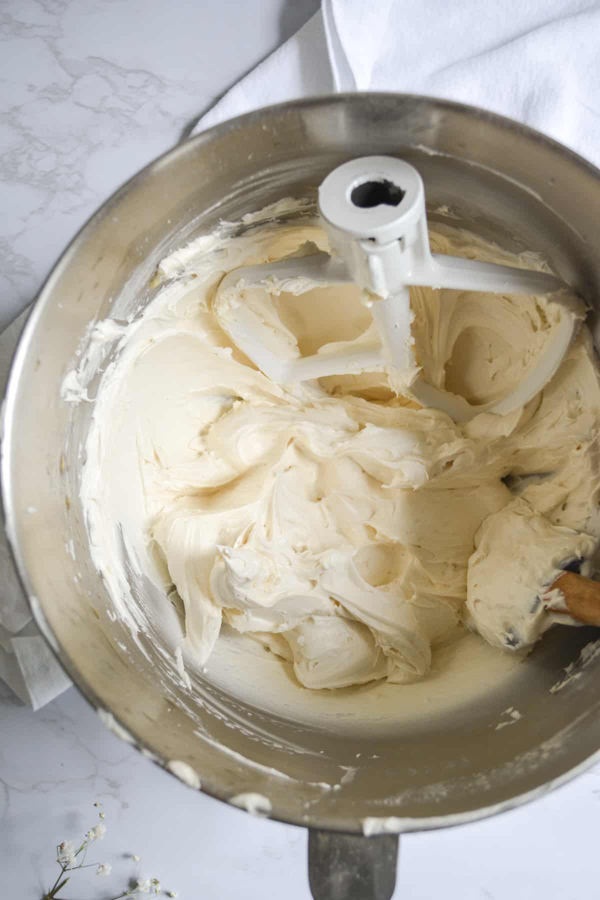 Finished vegan maple bourbon buttercream frosting in a metal bowl with the mixer paddle in it.