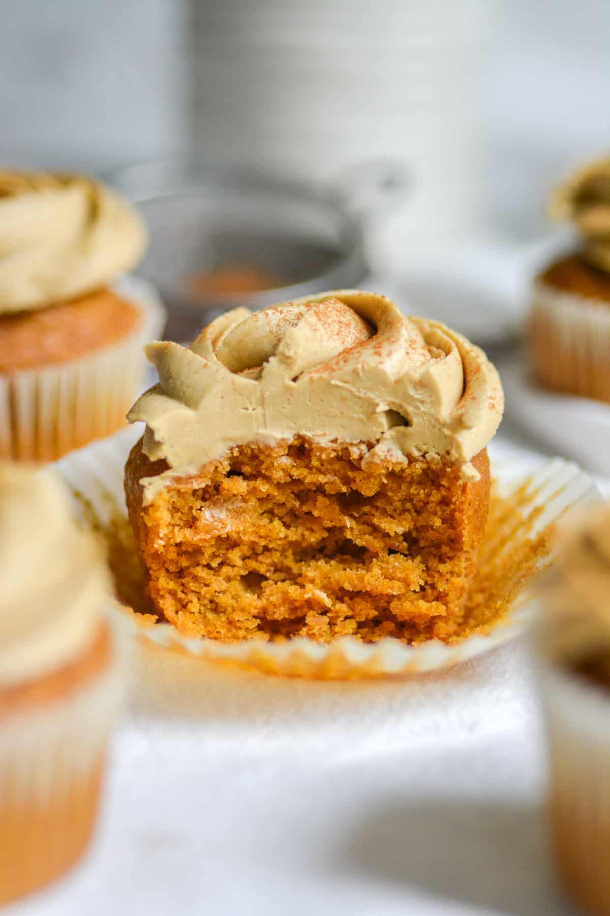 A vegan pumpkin chai cupcake with a bite taken out of it sitting in a cupcake wrapper.