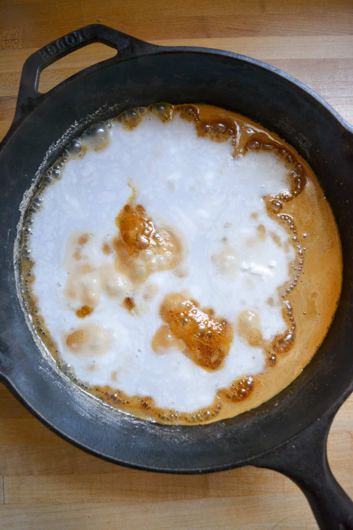 Coconut milk added into the caramelized sugar in a black skillet.