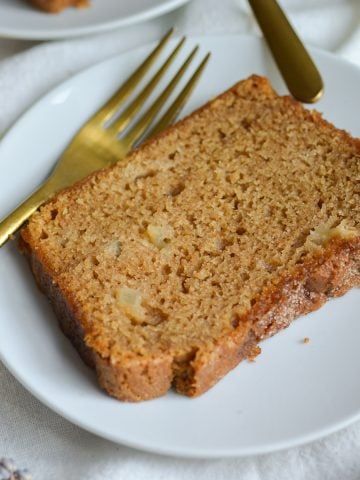 Vegan Apple Cinnamon Crunch Bread slice on a white plate with a gold fork.