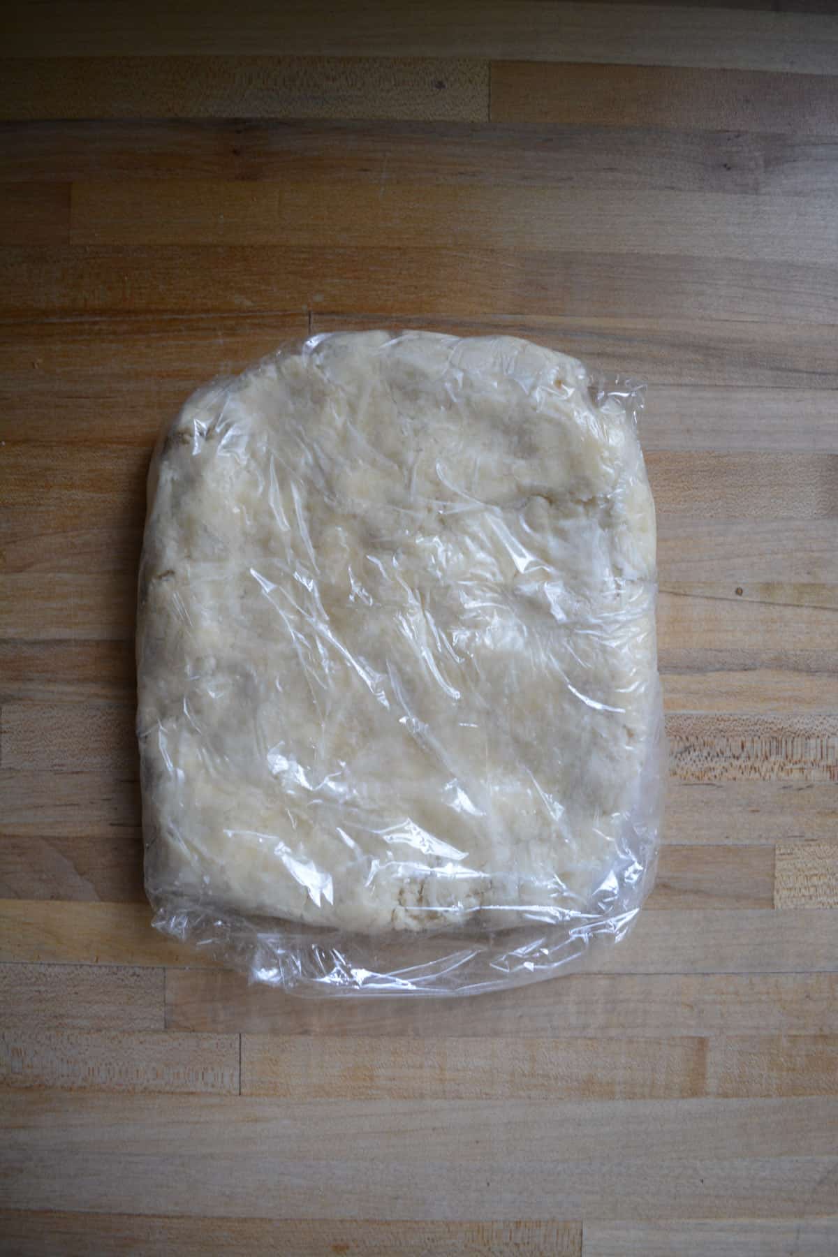 Pie dough flattened into a disc and wrapped in plastic wrap.