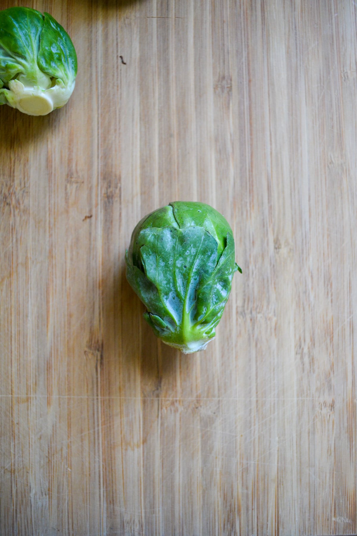 A brussels sprout on a wooden cutting board.