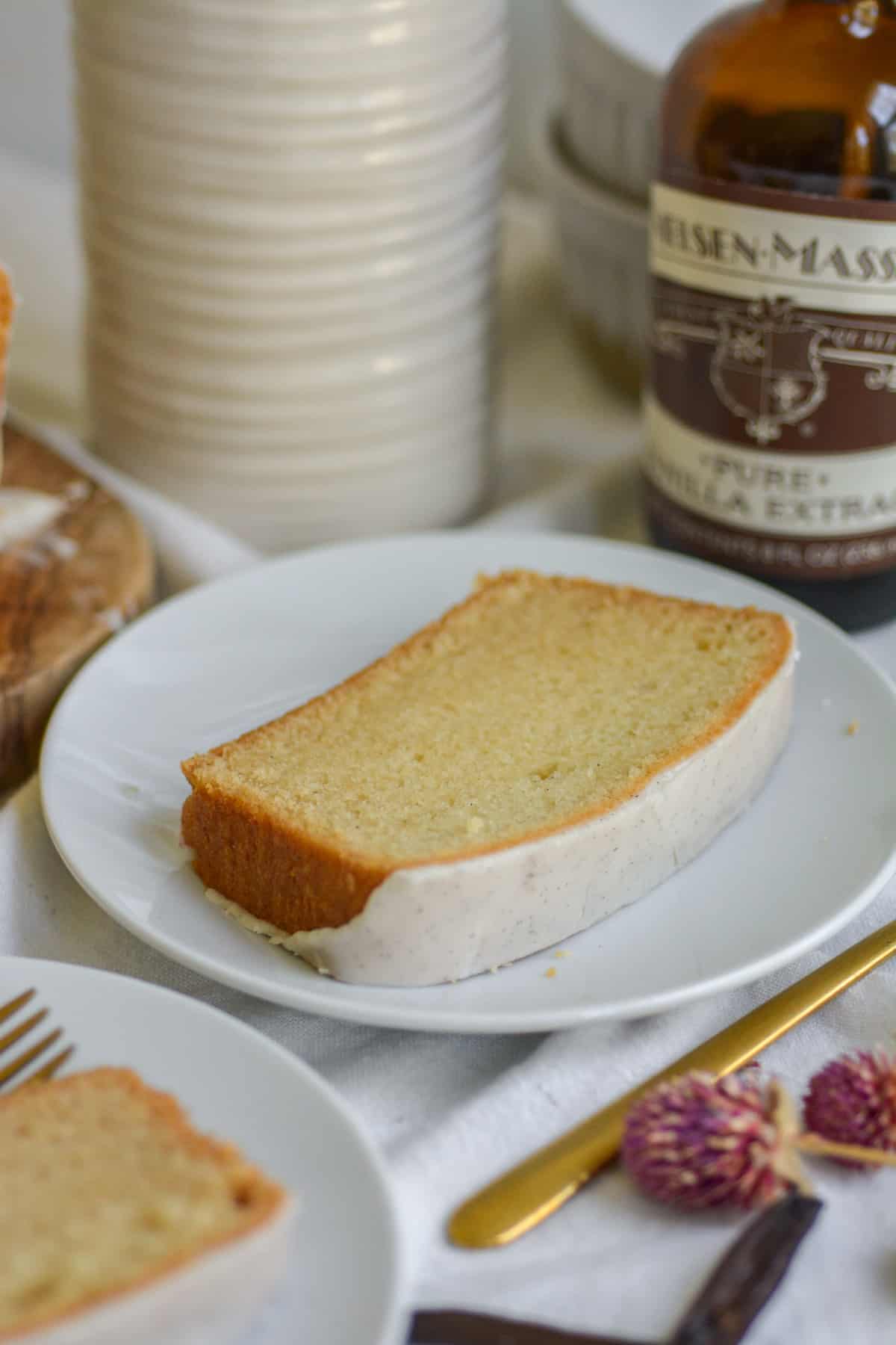 A slice of vegan pound cake on a white plate with a bottle of vanilla extract in the background.