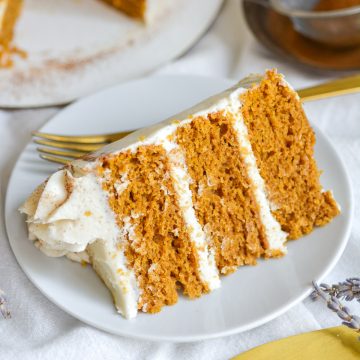 A slice of Vegan Pumpkin Spice Layer Cake on a small white plate on a white cloth.