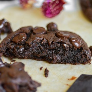 A broken open single serving vegan double chocolate cookie on parchment paper with pieces of chocolate in the foreground.