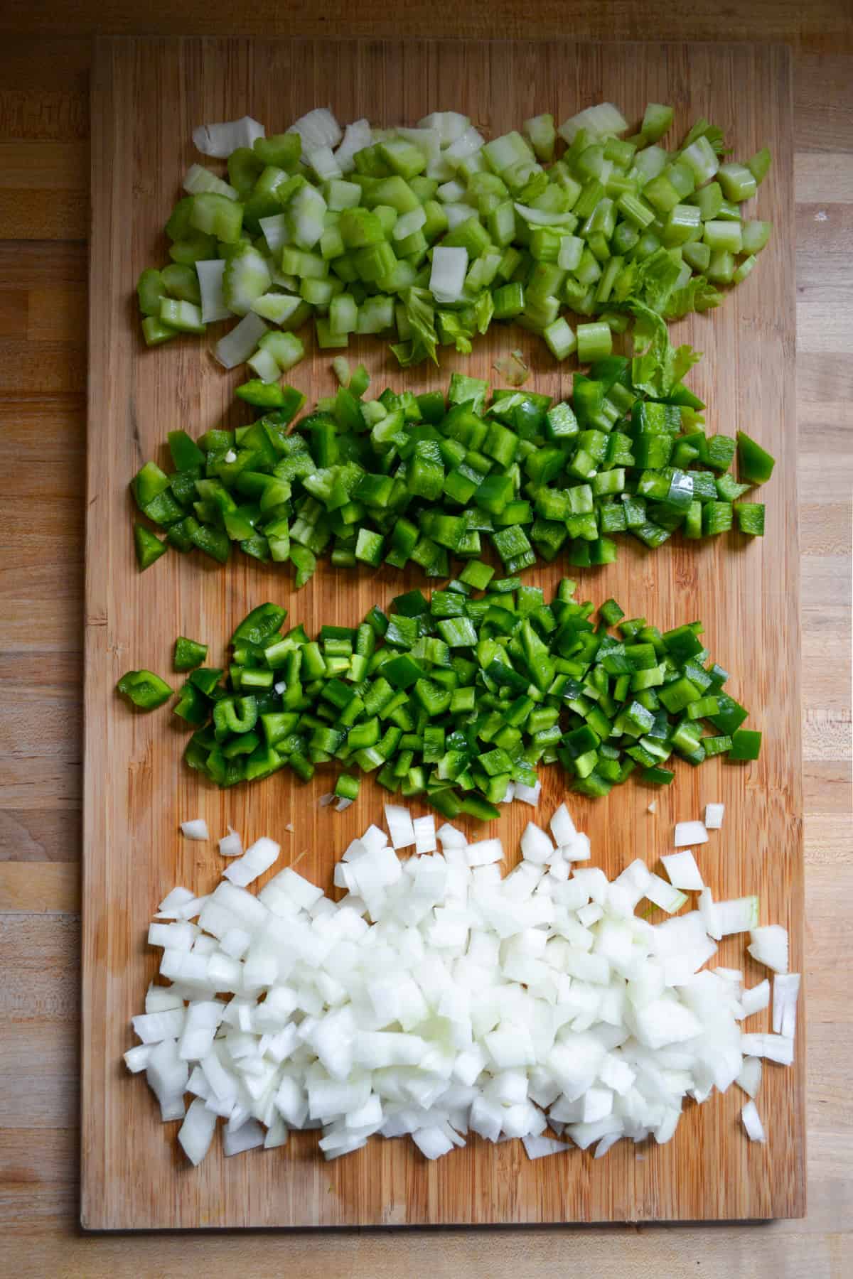 Overhead photo of onion, celery, green bell pepper and poblano pepper chopped up on a cutting board.