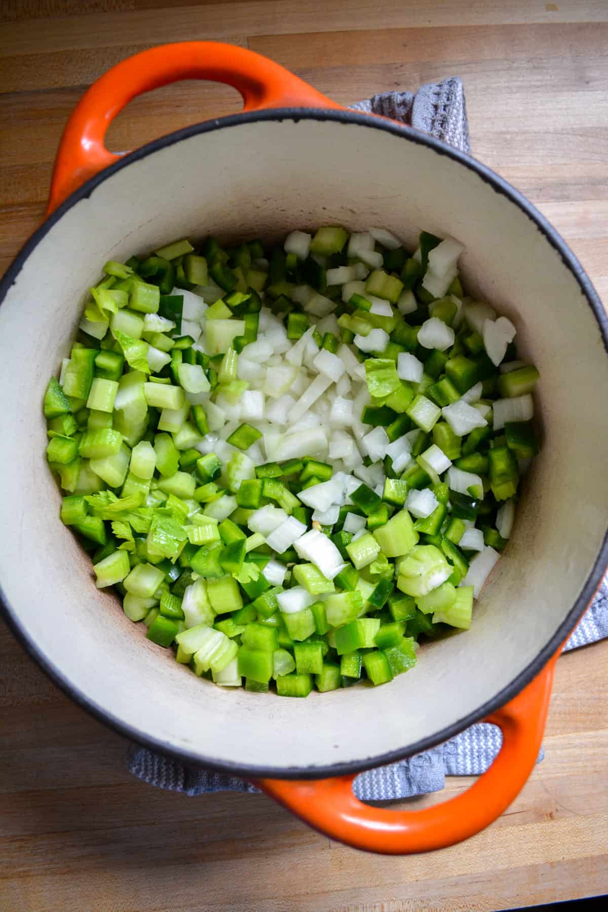 Overhead photo of onion, celery, green bell pepper and poblano pepper in a large Dutch oven.