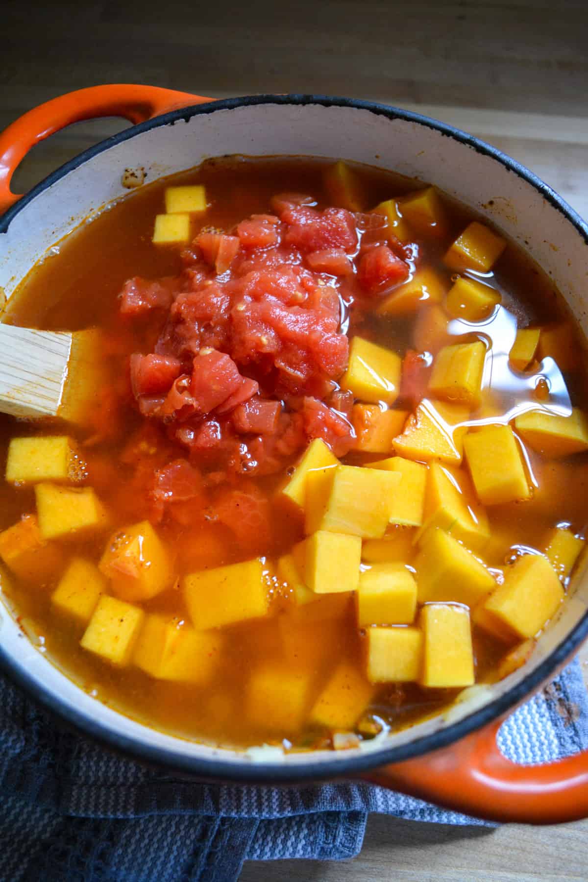 Overhead photo of diced tomatoes, butternut squash and vegetable stock added into the pot.