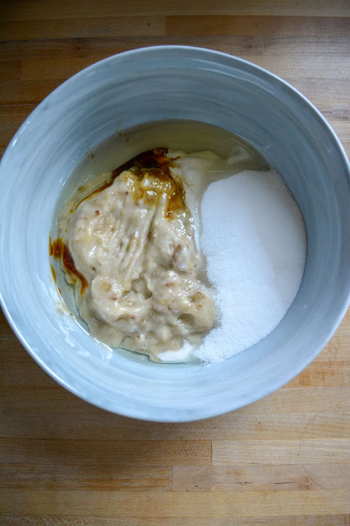 Overhead photo of sugar, mashed banana, vegan sour cream, oil and vanilla in a bowl.