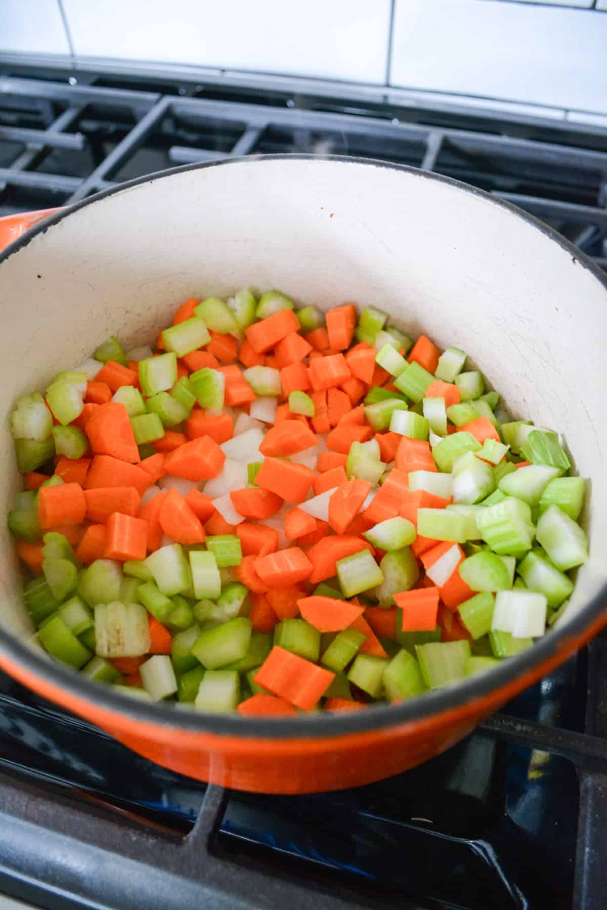 Onions, carrots and celery sautéing in an orange pot.