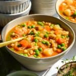 A bowl of vegan barley vegetable soup with a spoon in it.