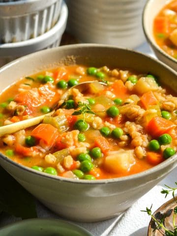 A bowl of vegan barley vegetable soup with a spoon in it.