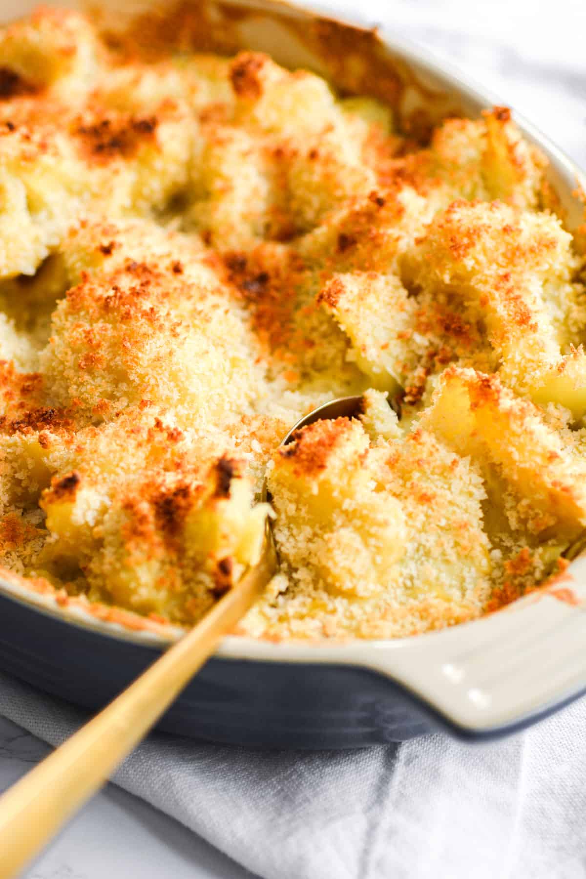 Vegan Cheesy Cauliflower Casserole in a blue baking dish with a gold spoon in it.