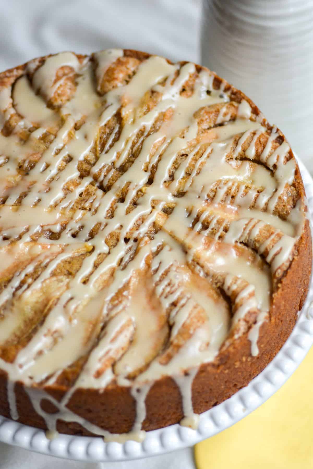 Vegan Pear Ginger Cake drizzle with maple glaze on a white cake stand.