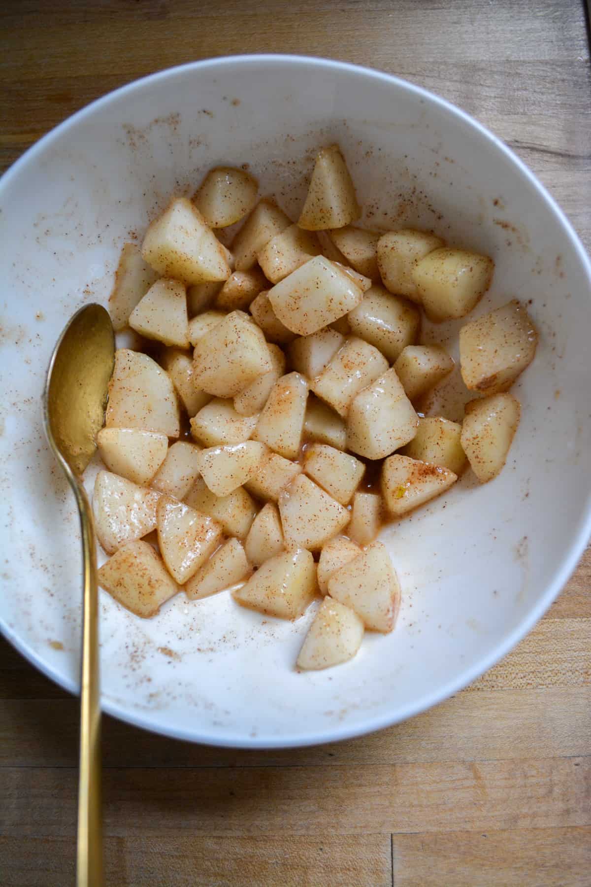 Pears mixed with cinnamon, cornstarch and lemon juice in a white bowl.